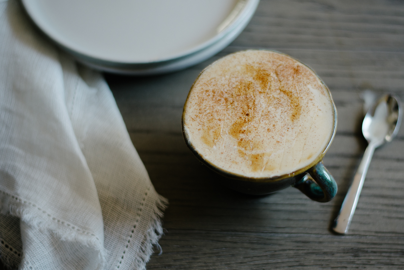 honey cinnamon latte in emerald green mug on gray wooden table with ivory napkin