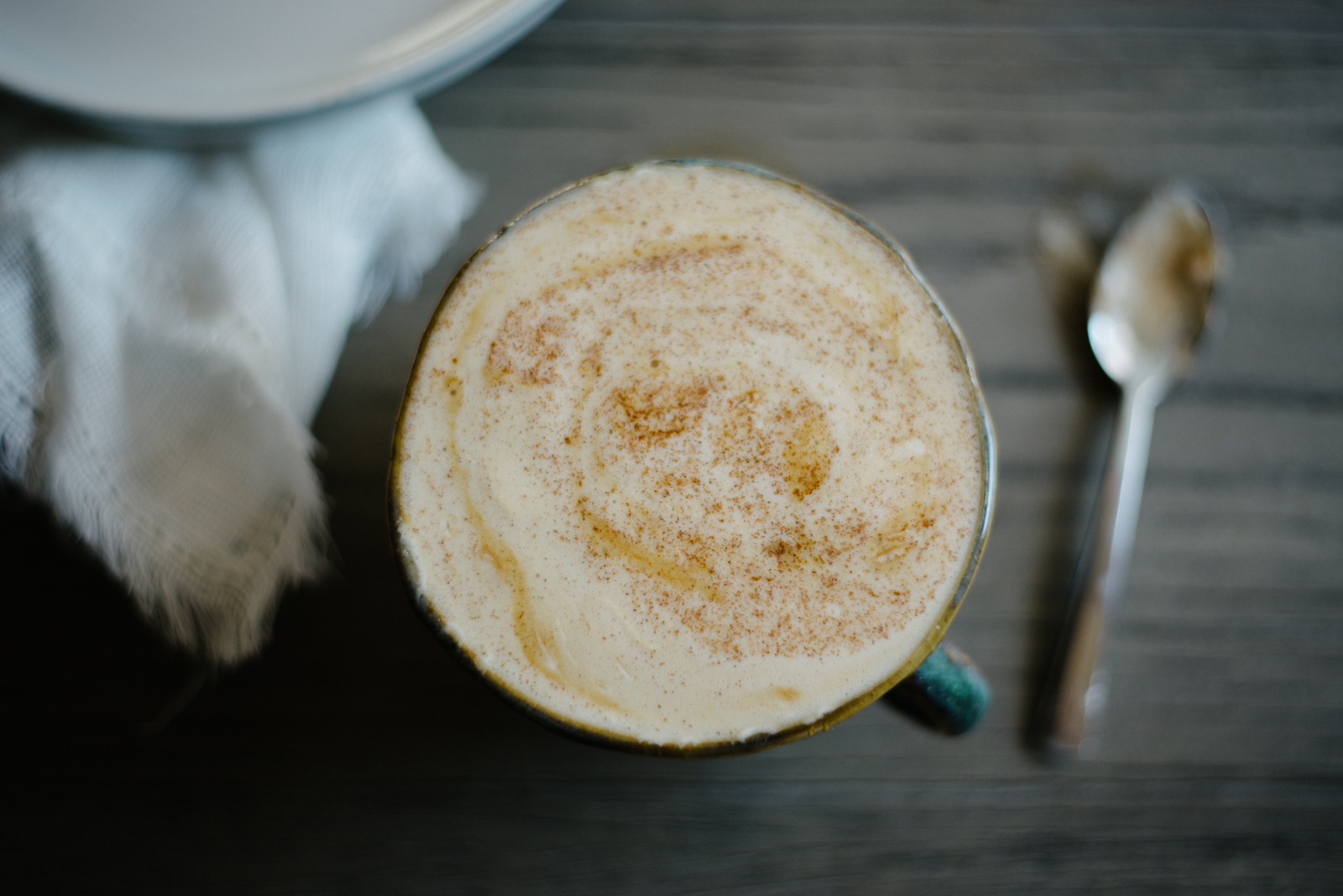 honey cinnamon latte in emerald green coffee mug on wooden table with silver spoon