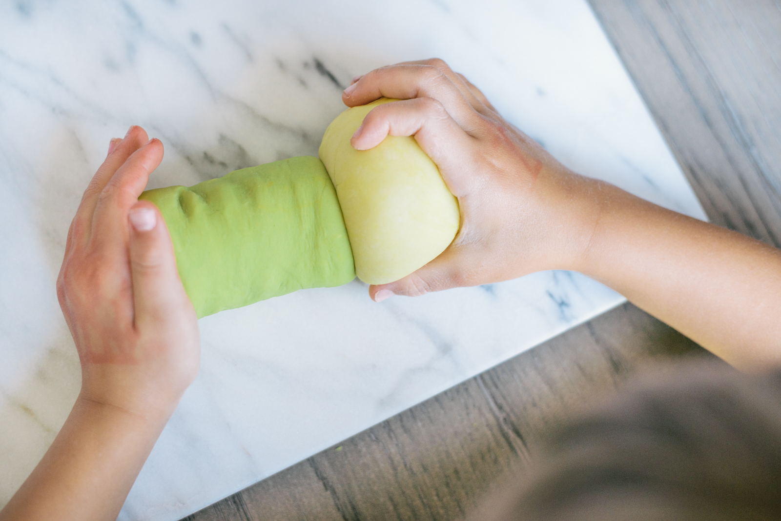 child's hands playing with naturally dyed green and yellow play dough on marble