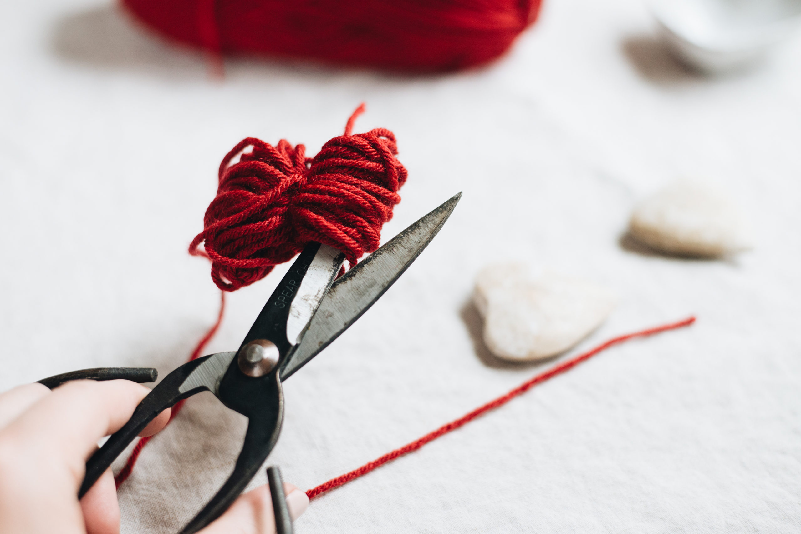 snip heart pom poms with red yarn and scissors casey wiegand